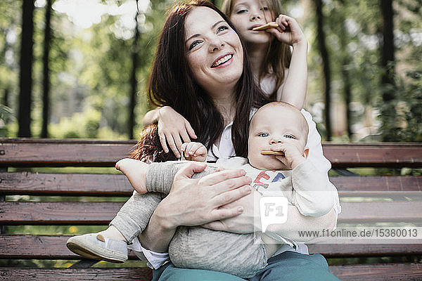Lächelnde Mutter mit ihren beiden Kindern beim Keksessen im Park