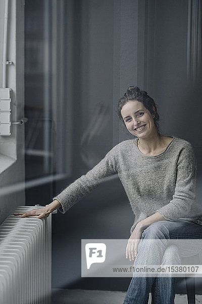 Porträt einer lächelnden jungen Frau  die zu Hause neben der Heizung sitzt