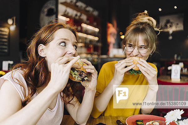 Two female friends eating burger in a restaurant