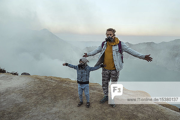 Father and son with respirator masks standing at the edge of volcano Ijen  Java  Indonesia