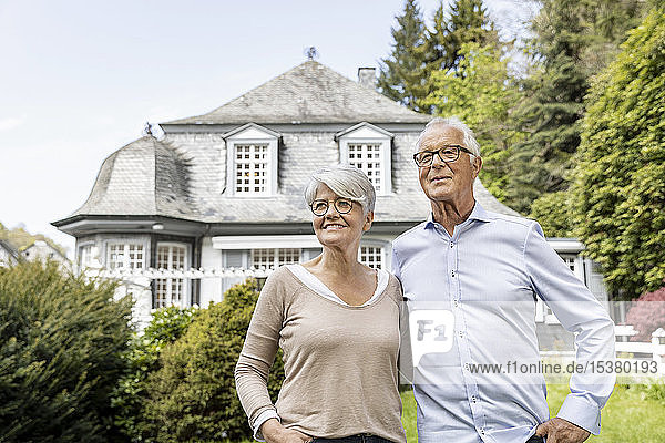 Lächelndes älteres Ehepaar steht im Garten seines Hauses