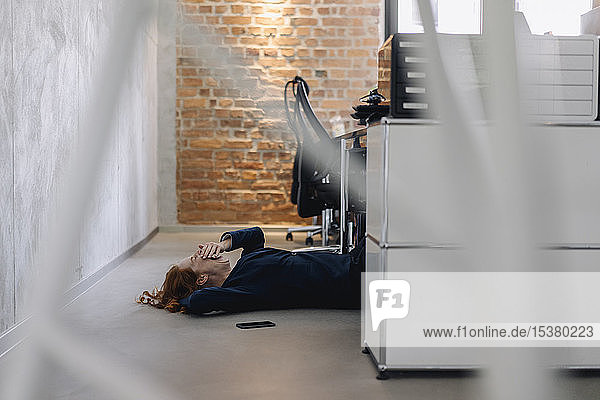 Müde Geschäftsfrau liegt im Büro auf dem Boden
