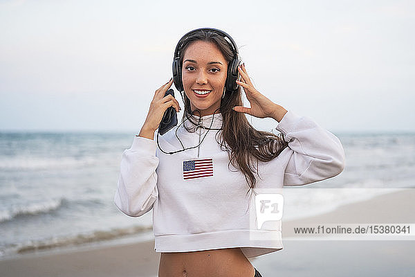 Portrait of young woman listening to music with headphones on the beach