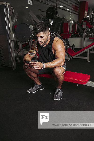 Muskulöser Mann überprüft Smartphone im Fitnessstudio