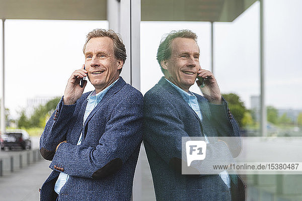 Portrait of smiling senior businessman on the phone at glass front