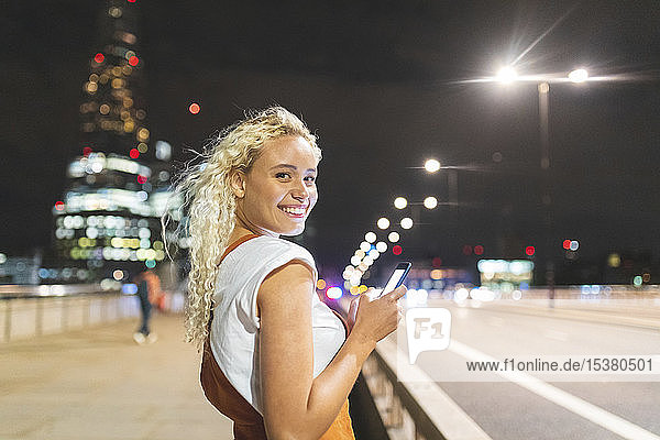 Young woman in London at night and using her smartphone