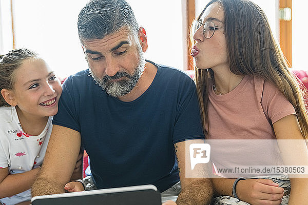 Father with two daughters looking at tablet on couch at home