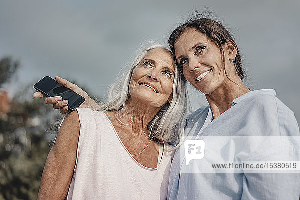 Mutter und Tochter verbringen einen Tag am Meer mit einem Smartphone in der Hand