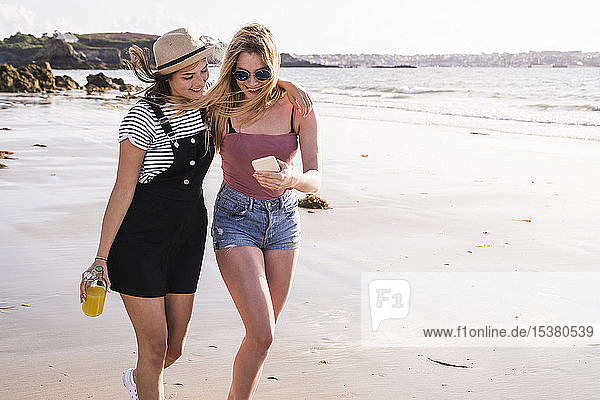 Two girlfriends having fun  walking on the beach  taking smartphone selfies