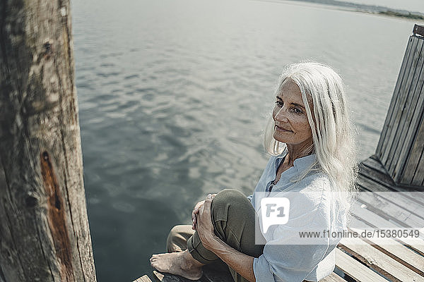 Ältere Frau sitzt auf einem Steg und entspannt sich am Meer