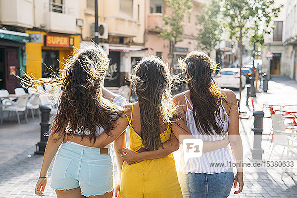 Rückansicht von drei Freundinnen  die in der Stadt spazieren gehen