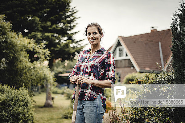 Stolze Hausbesitzerin steht mit einem Spaten in ihrem Garten