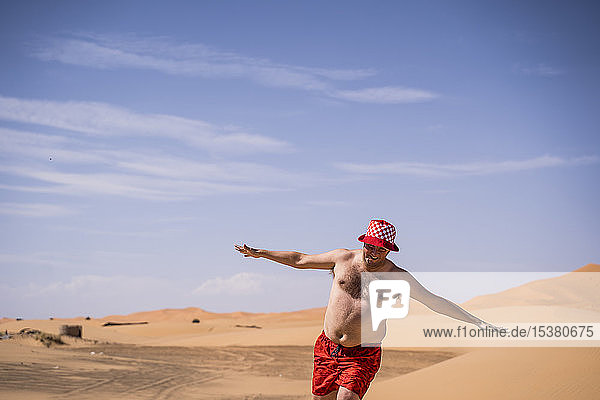 Glücklicher übergewichtiger Mann mit Badeshorts läuft in der Wüste von Marokko