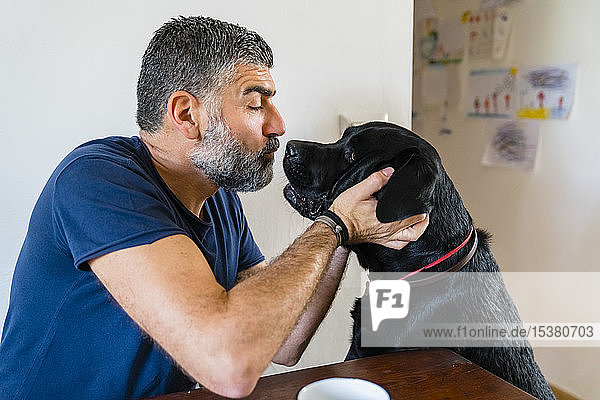 Mann spielt zu Hause mit Hund am Tisch
