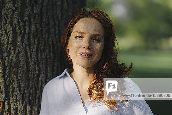 Porträt einer rothaarigen Frau an einem Baum in einem Park