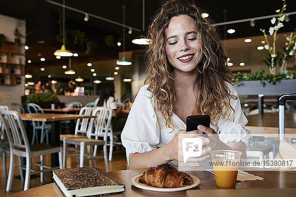 Smiling young woman using smartphone in a cafe while having breakfast