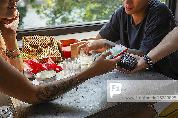 Junge Frau bezahlt Rechnung mit Smartphone im Café