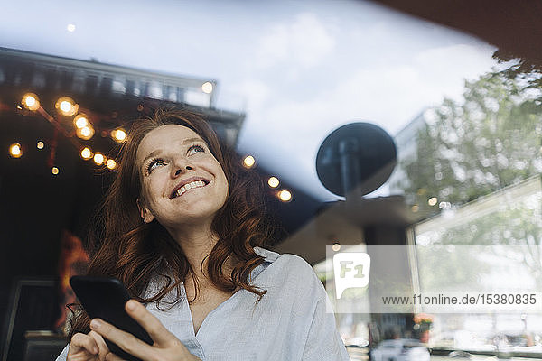Glückliche rothaarige Frau mit Handy in einem Cafe