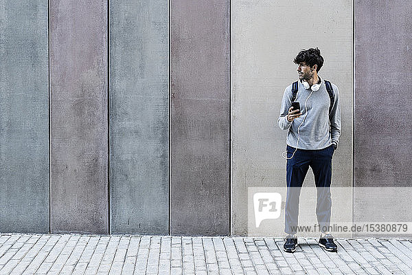 Man with cell phone and headphones standing in front of awall