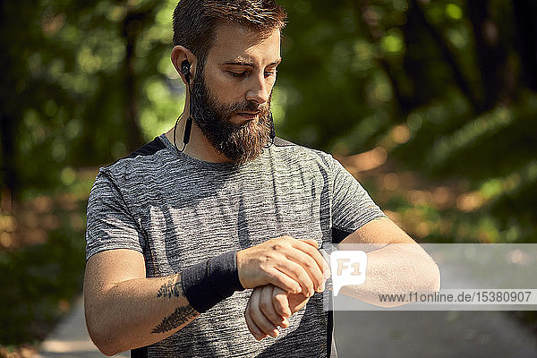 Porträt eines sportlichen Mannes mit Kopfhörern im Wald beim Prüfen seiner Smartwatch