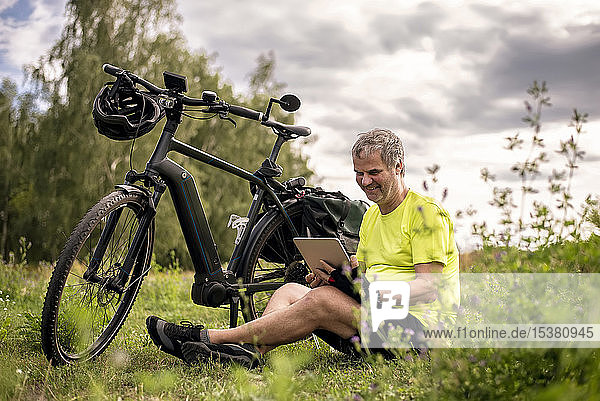 Reifer Mann benutzt digitales Tablett während seiner Fahrradtour mit einem E-Bike
