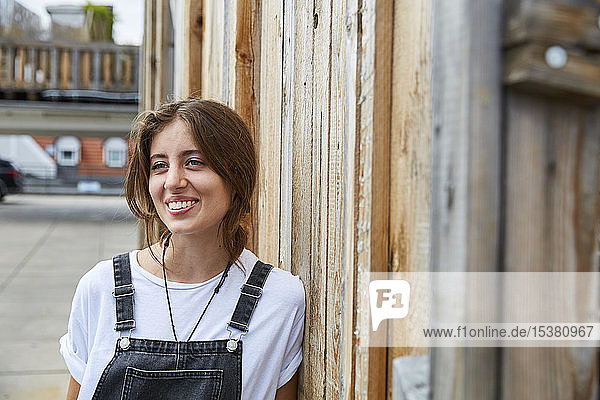 Portrait of smiling young woman leaning agianst wooden fence