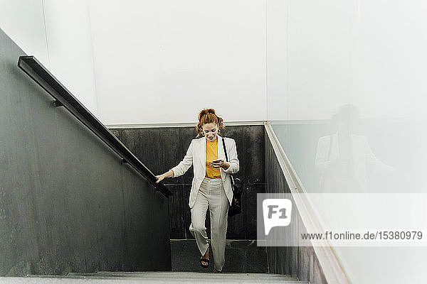 Businesswoman in white pant suit  ascending stairs  using smartphone