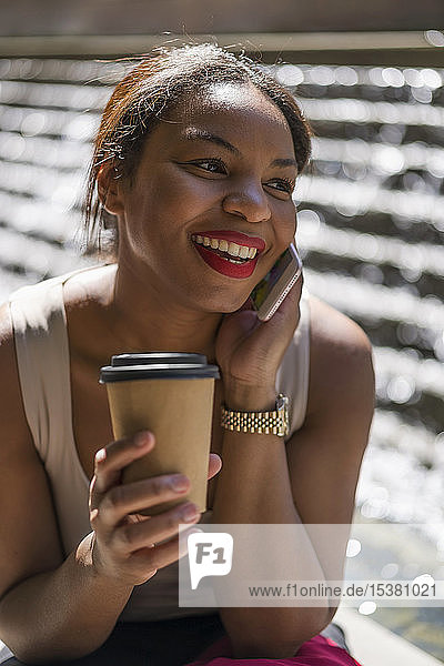 Portrait of happy woman with coffee to go on the phone  London  UK