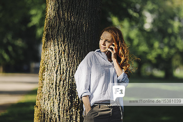 Rothaarige Frau telefoniert im Park
