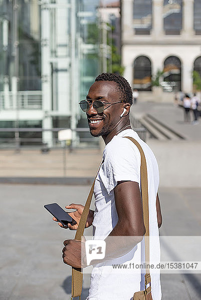 Lächelnder junger Mann benutzt Smartphone und Kopfhörer