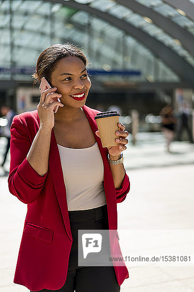 Portrait of smiling businesswoman with coffee to go on the phone  London  UK