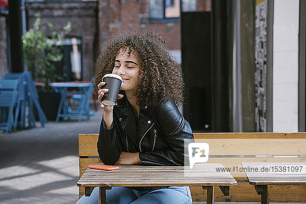 Porträt einer glücklichen Teenagerin  die im Straßencafé Kaffee zum Mitnehmen genießt