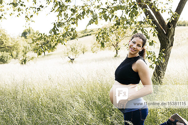 Junge schwangere Frau mit Babybauch  auf einer Wiese stehend