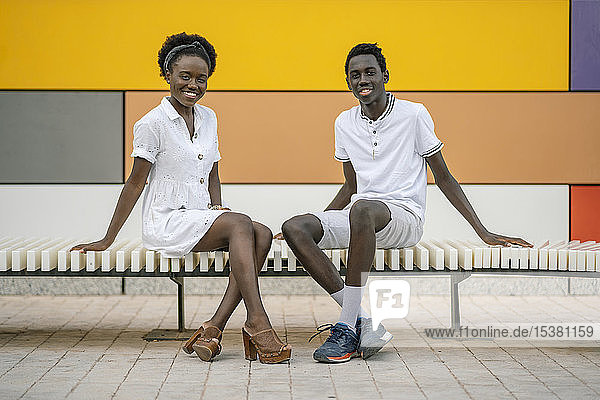 Portrait of happy young couple sitting on bench outdoors