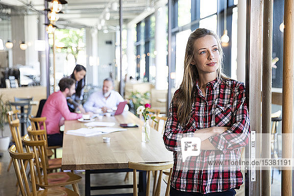 Portrait of casual businesswoman in a cafe with colleagues having a meeting in background