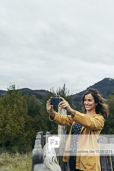 Young woman wearing yellow coat taking a photo with her smartphone