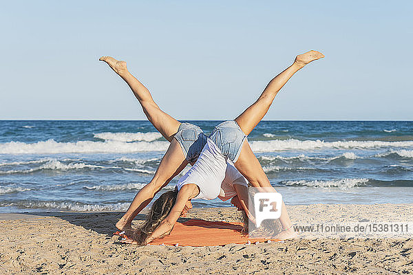 Zwei Frauen praktizieren Acro Yoga am Strand  nach unten gerichtete Hundestellung