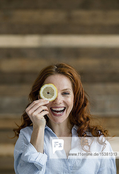 Porträt einer lachenden rothaarigen Frau  die das Auge mit einer Zitronenscheibe bedeckt