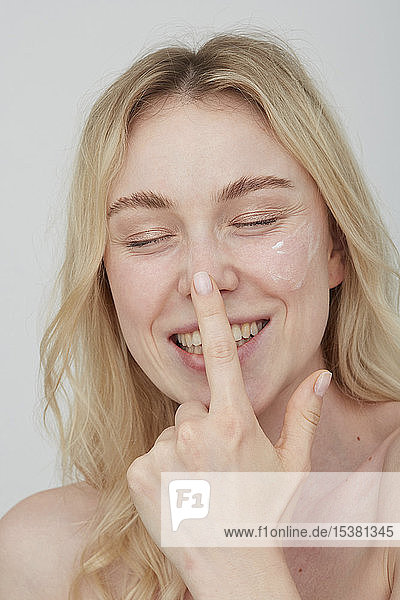 Portrait of laughing young woman applying cream on her face