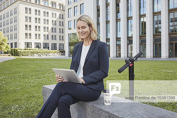 Geschäftsfrau sitzt in der Stadt mit Tablette an einer Wand