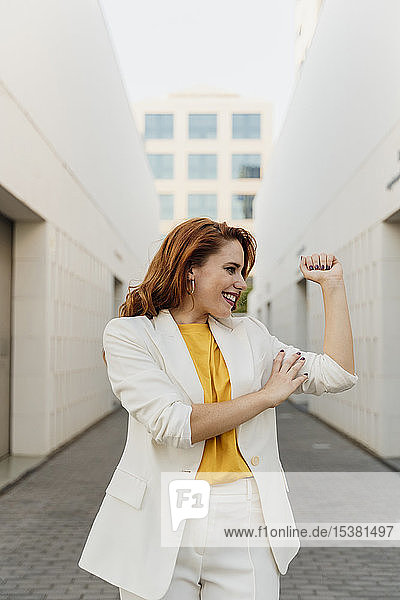 Energische Geschäftsfrau im weißen Hosenanzug  die ihre Muskeln spielen lässt