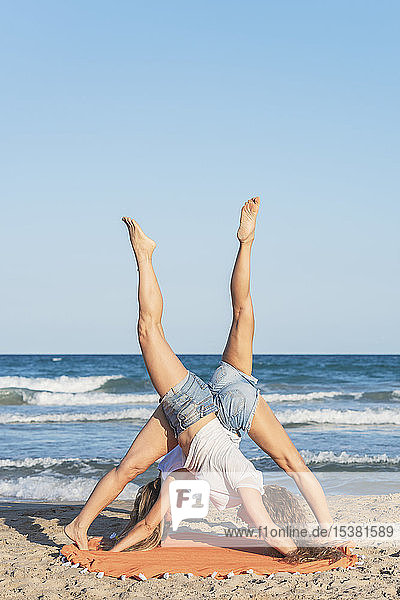 Zwei Frauen praktizieren Acro Yoga am Strand  nach unten gerichtete Hundestellung