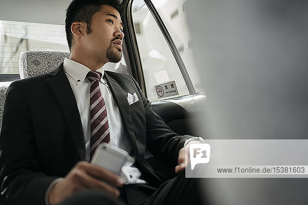 Young businessman with cell phone in a taxi looking out of window