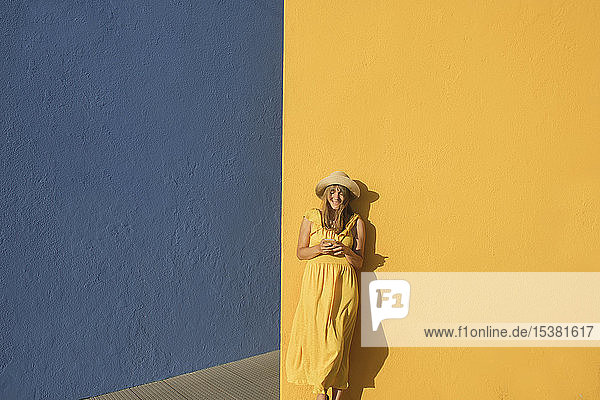 Frau in einem gelben Kleid mit Smartphone vor gelben und blauen Wänden