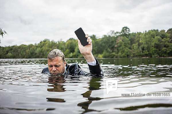 Geschäftsmann hält Mobiltelefon in einem See