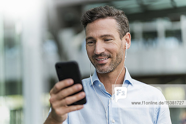 Smiling businessman with earphones and cell phone in the city