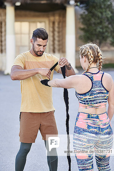 Fitnesstrainer übt Boxunterricht mit einer jungen Frau im Freien in der Stadt beim Anlegen eines Verbandes