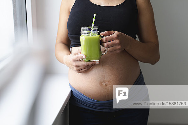 Junge schwangere Frau trinkt frischen und gesunden grünen Smoothie