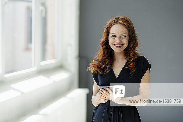 Porträt einer zufriedenen rothaarigen Geschäftsfrau mit digitalem Tablet in einem Loft