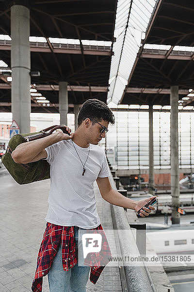 Junger Mann wartet am Bahnhof und benutzt ein Smartphone